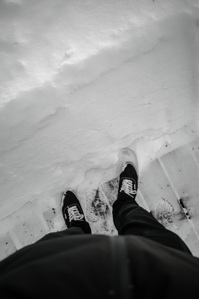 Dressed in a black pants and black and white sneakers the man standing in the snow
